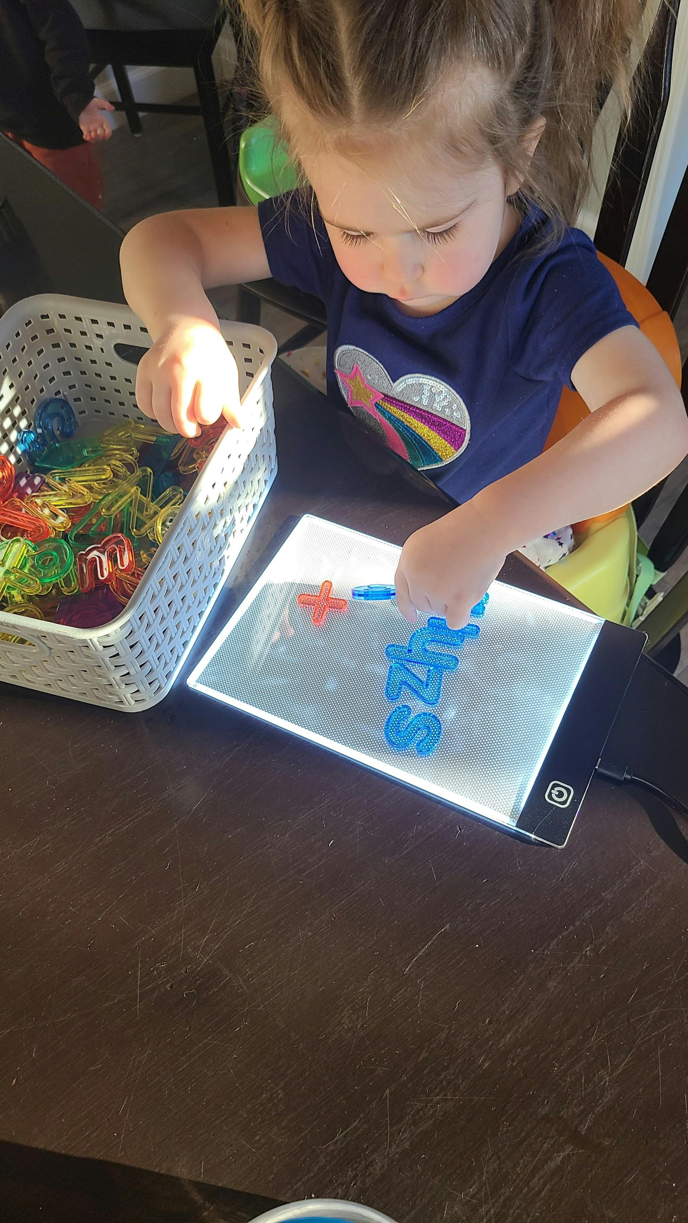 Child playing with colorful letter magnets on a light-up board