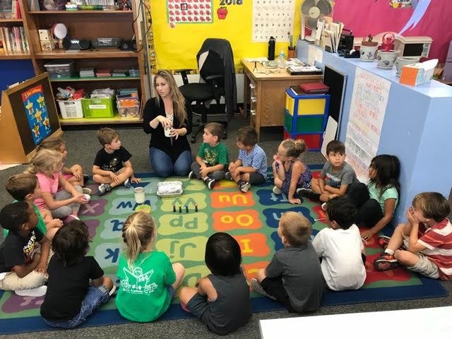 Adult and children sitting in a circle on a rug in a classroom