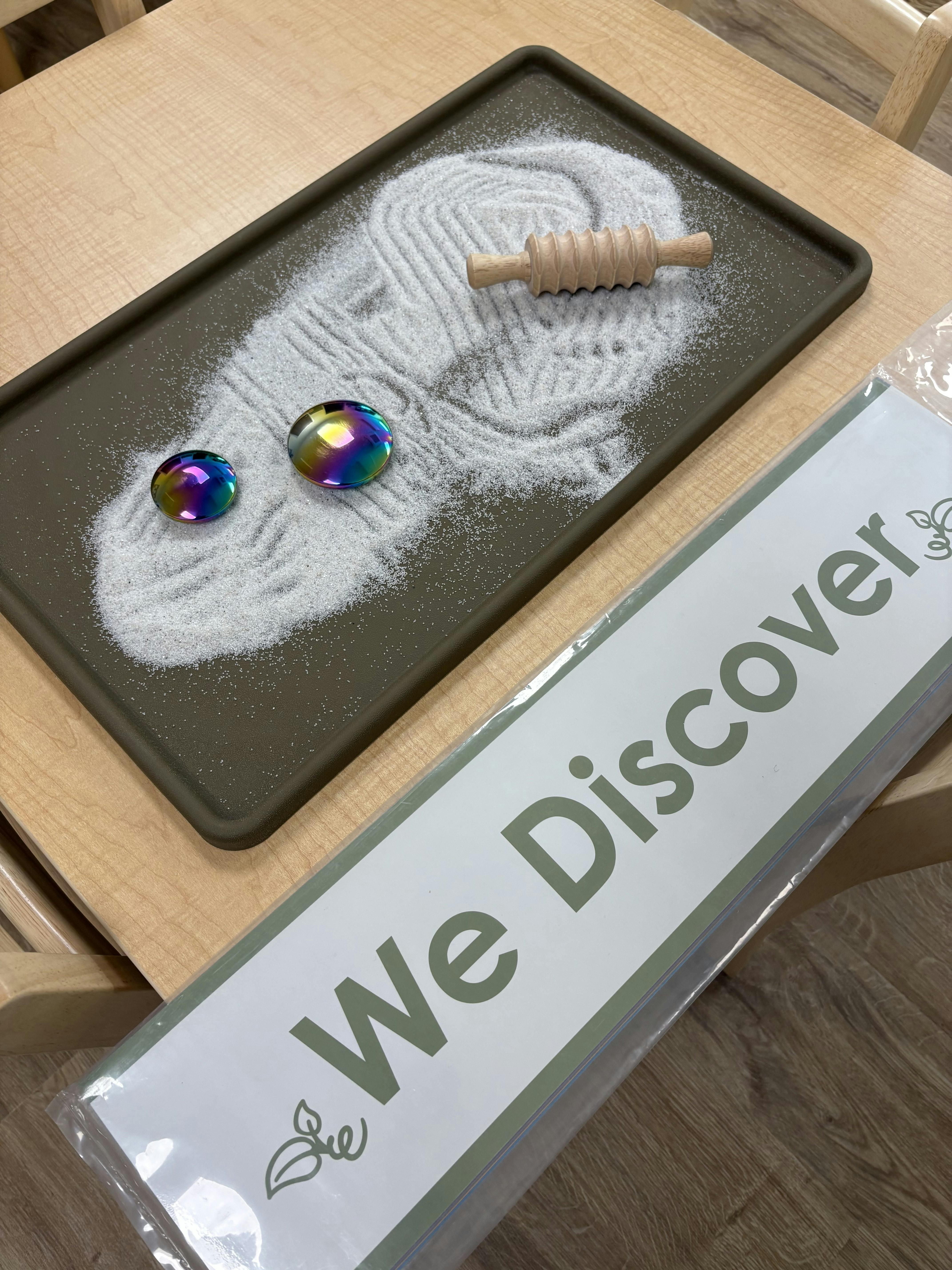 Tray with sand, a small rolling pin, and two iridescent stones