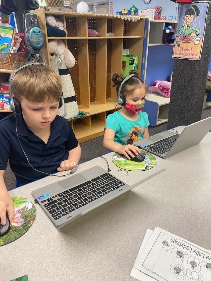 Two children wearing headphones and using laptops
