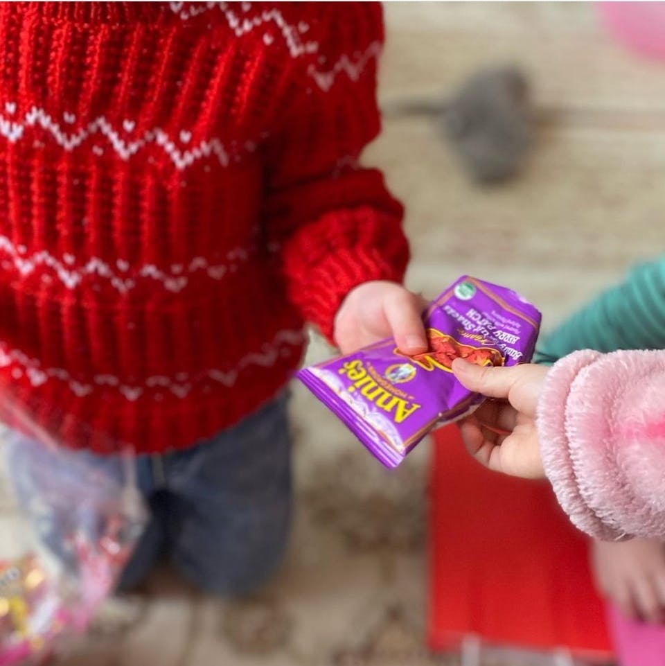 Child in red sweater giving purple snack bags to another child
