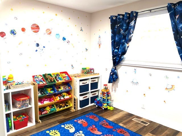 Child's room with space-themed wall decals, toy storage, and blue rug