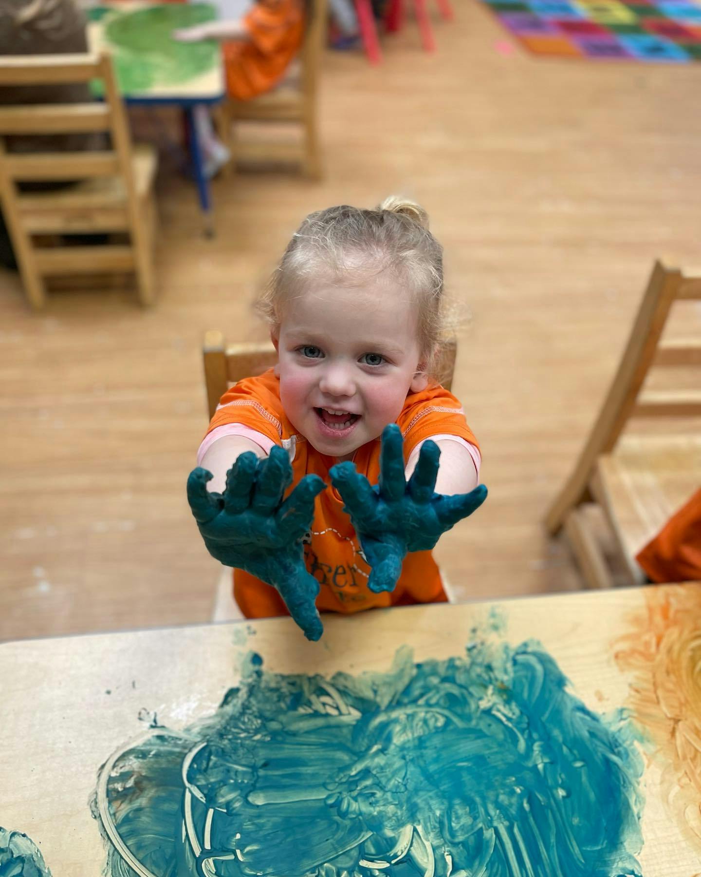 Child with blue paint on hands and table
