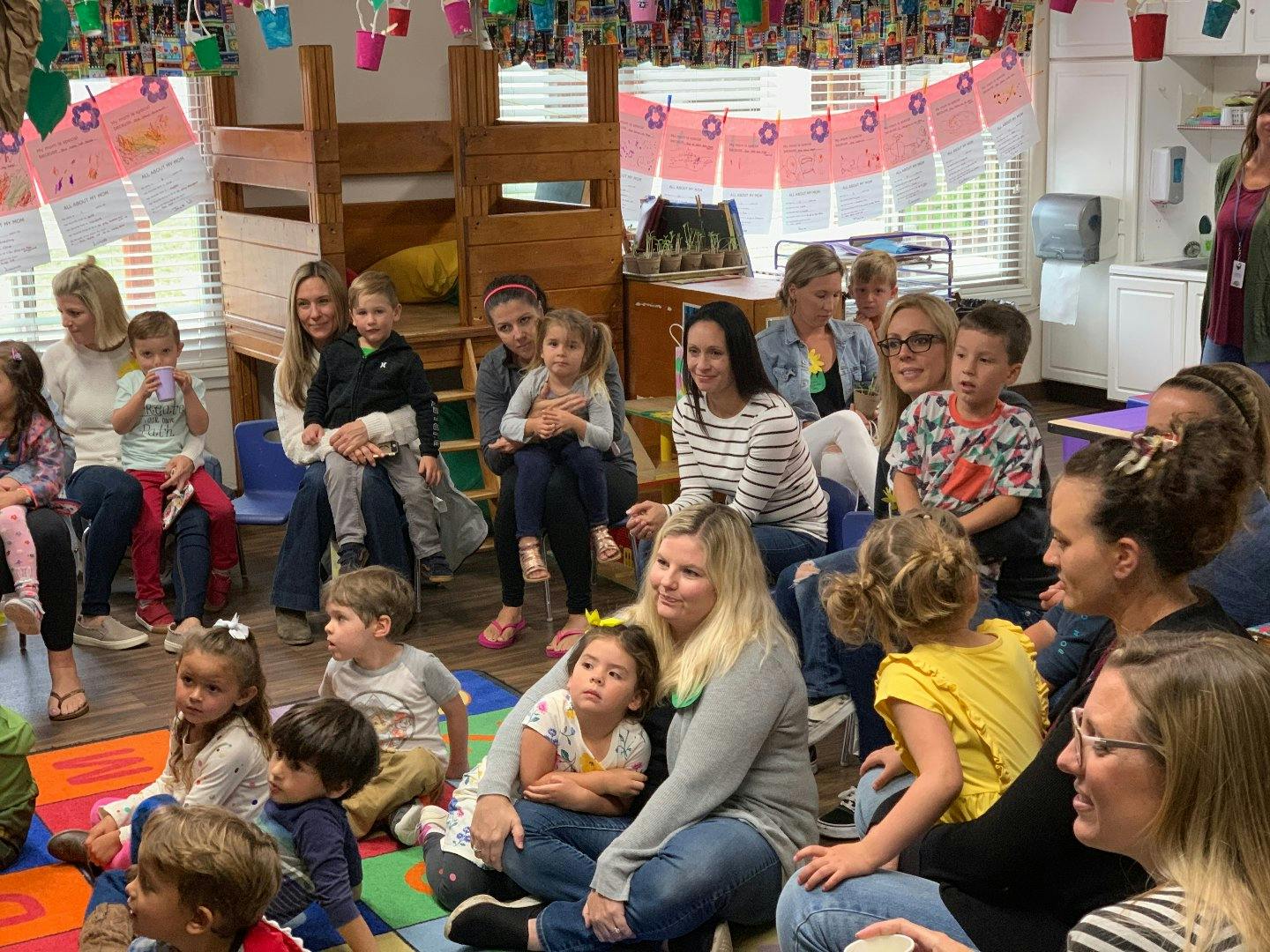 Adults and children sitting on the floor and chairs in a room