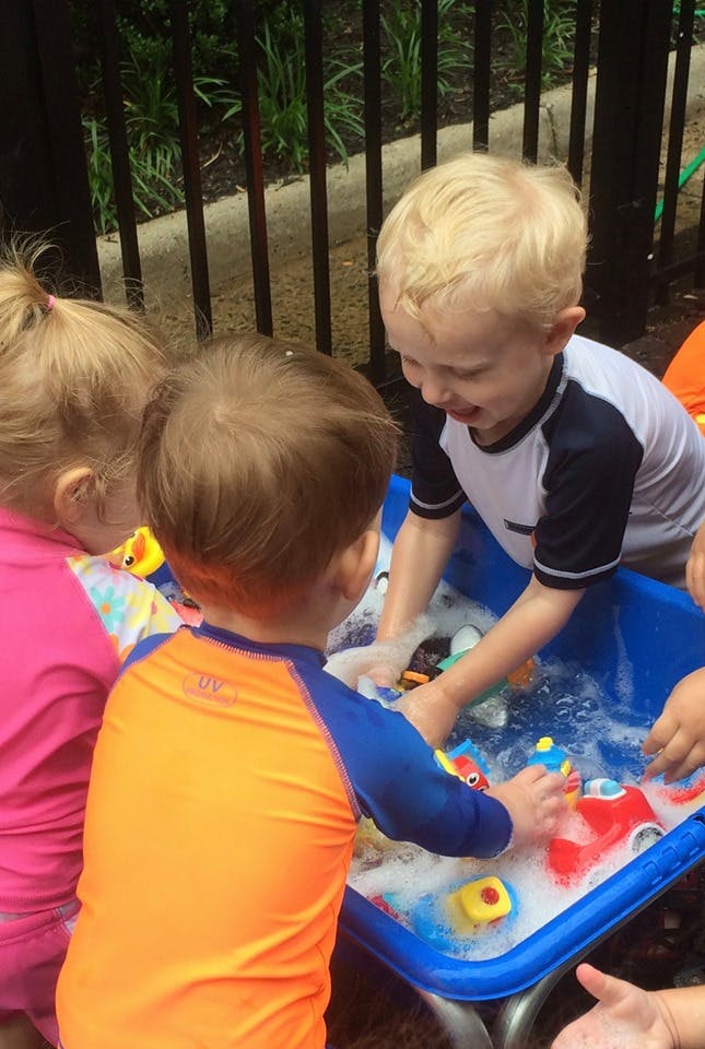 Three children playing with toys in a water table