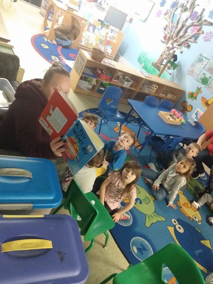 Person reading a book to a group of children in a classroom