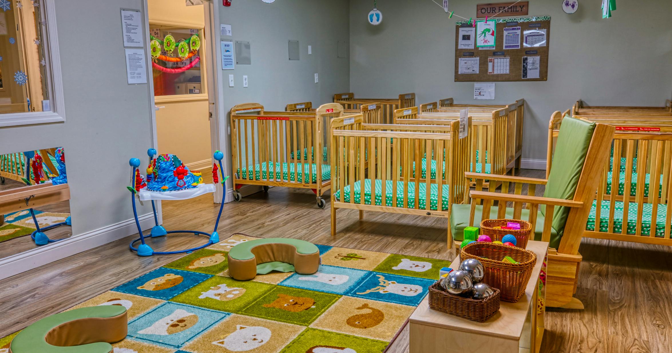 A room with multiple wooden cribs, a colorful playmat, and baby toys
