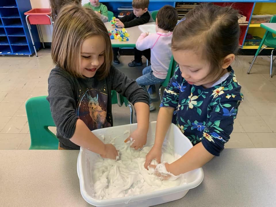 Two children playing with white dough in a classroom