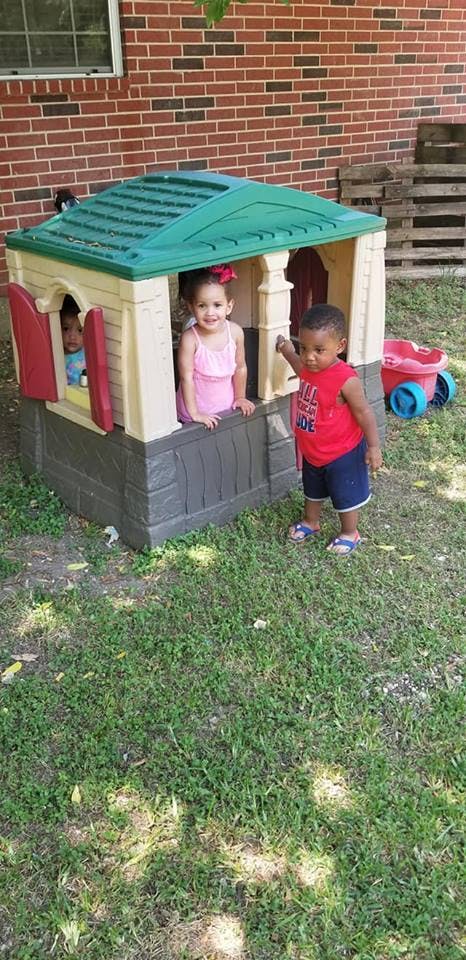 Two children playing in and around a toy playhouse