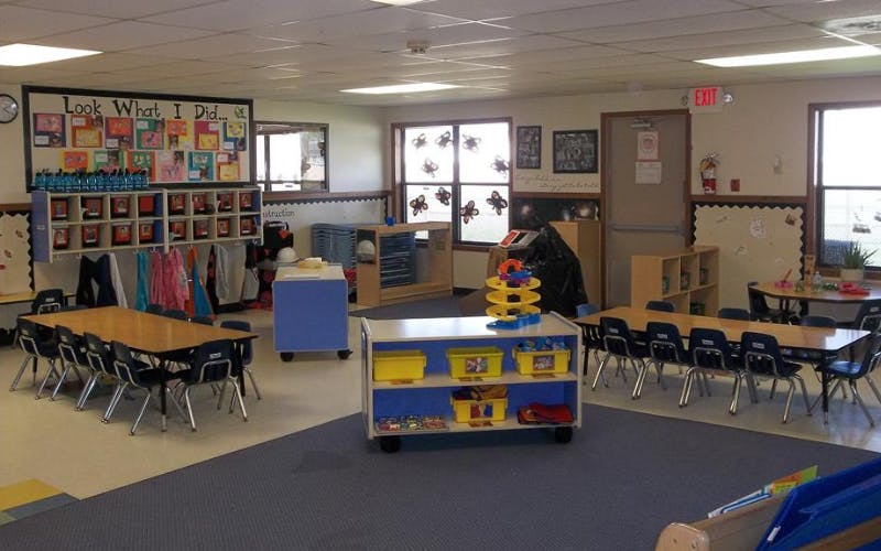 An empty early childhood classroom with small tables and chairs