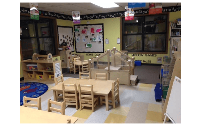Empty classroom with small tables and chairs, play structures, and alphabet on the wall