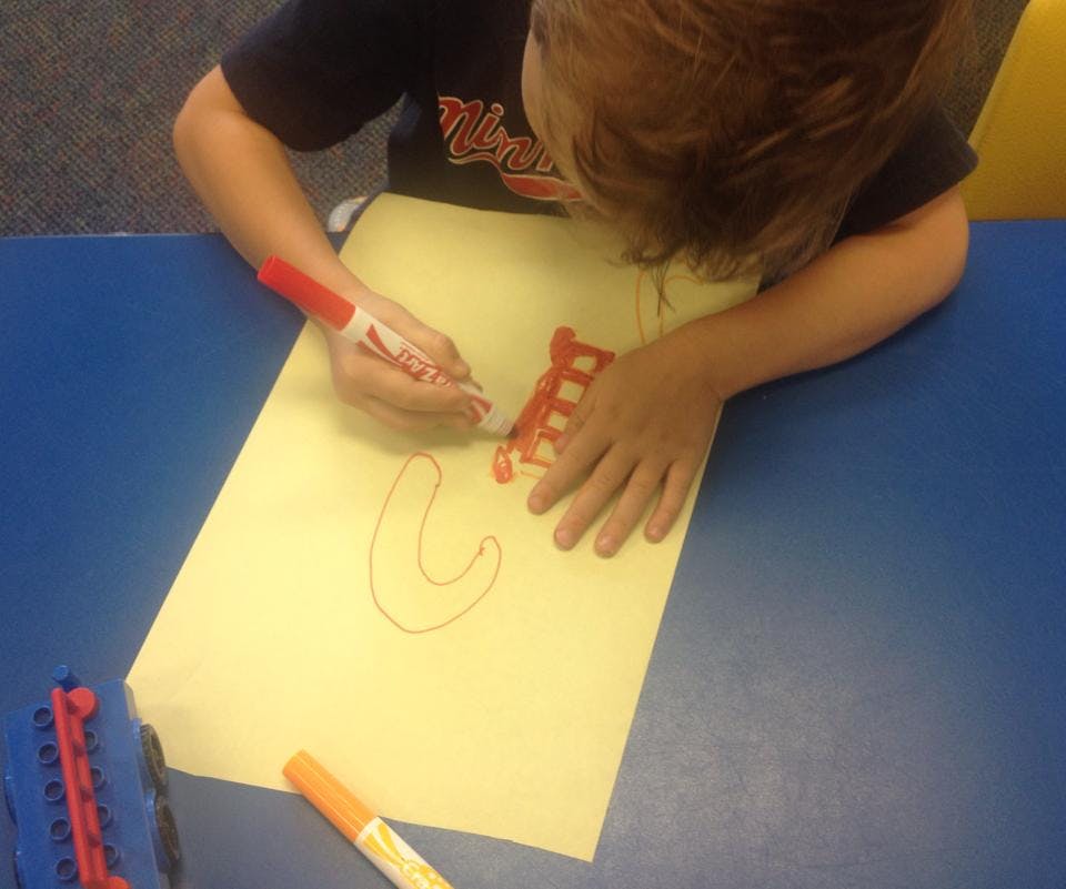 Child drawing on paper with a red marker