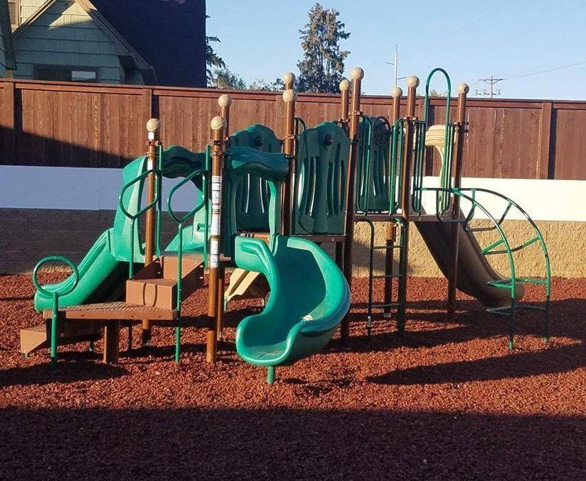 Playground with green slides and climbing structures on wood chips