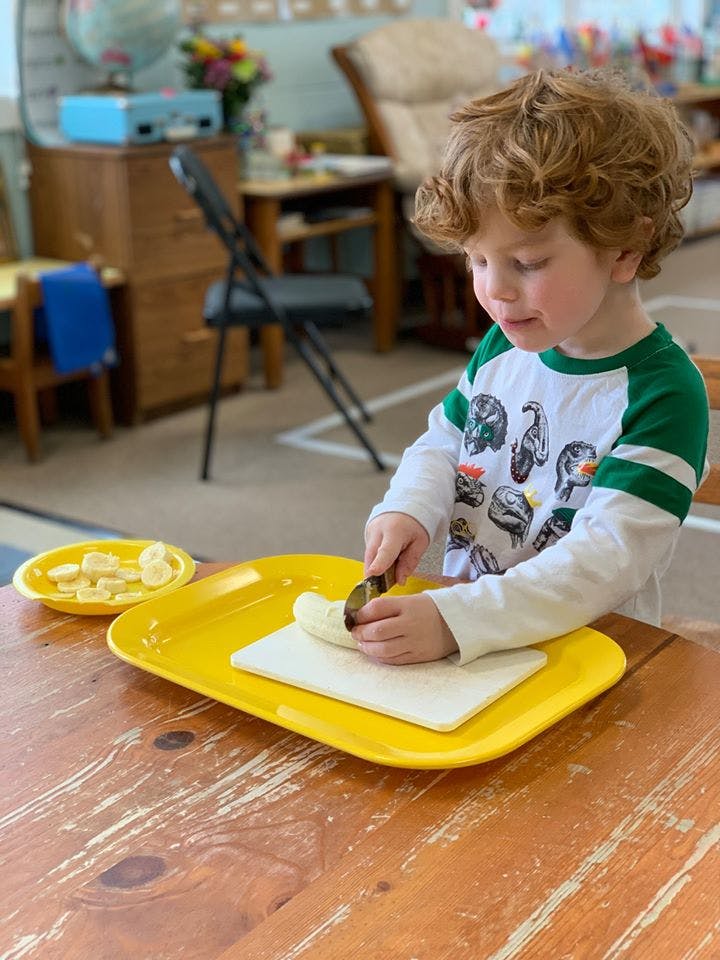 Child cutting a banana on a yellow tray