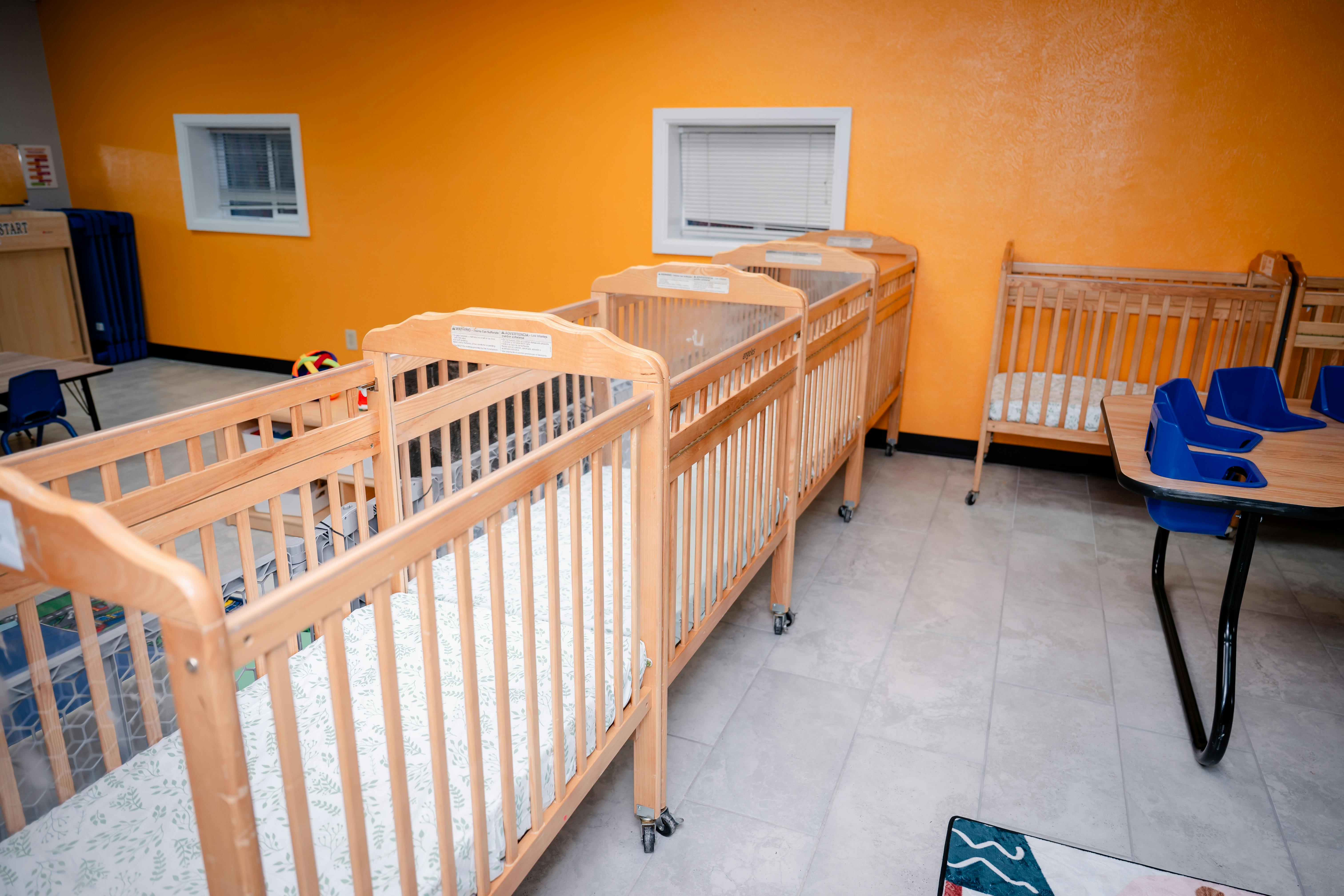 Multiple wooden cribs in a room with orange walls
