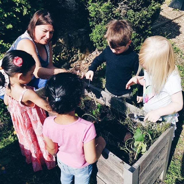 Person and three children looking into a wooden planter