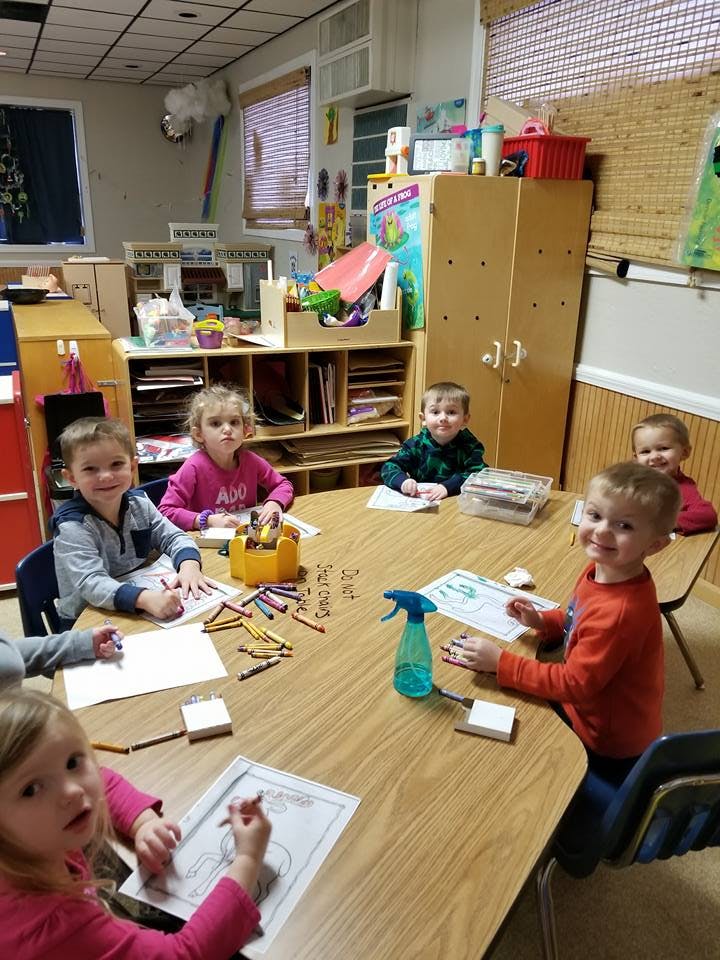Children sitting at a table coloring in a classroom