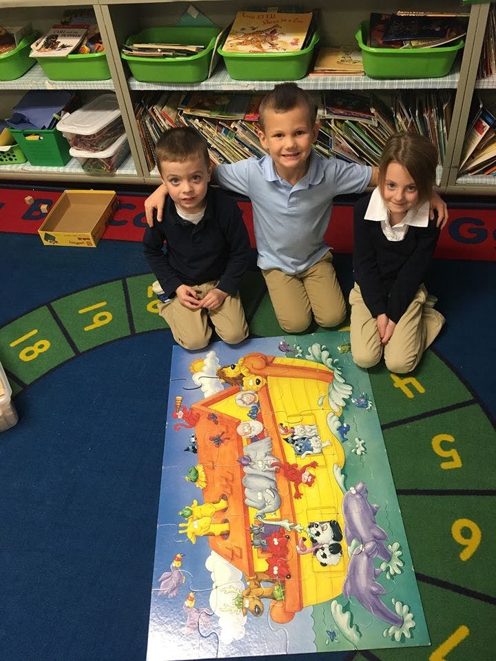 Three children kneeling around a large floor puzzle in a classroom