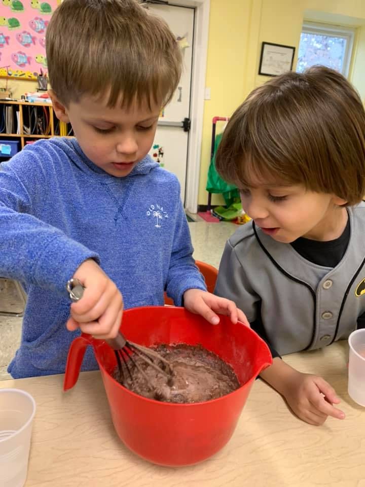 Two children mixing batter in a red bowl