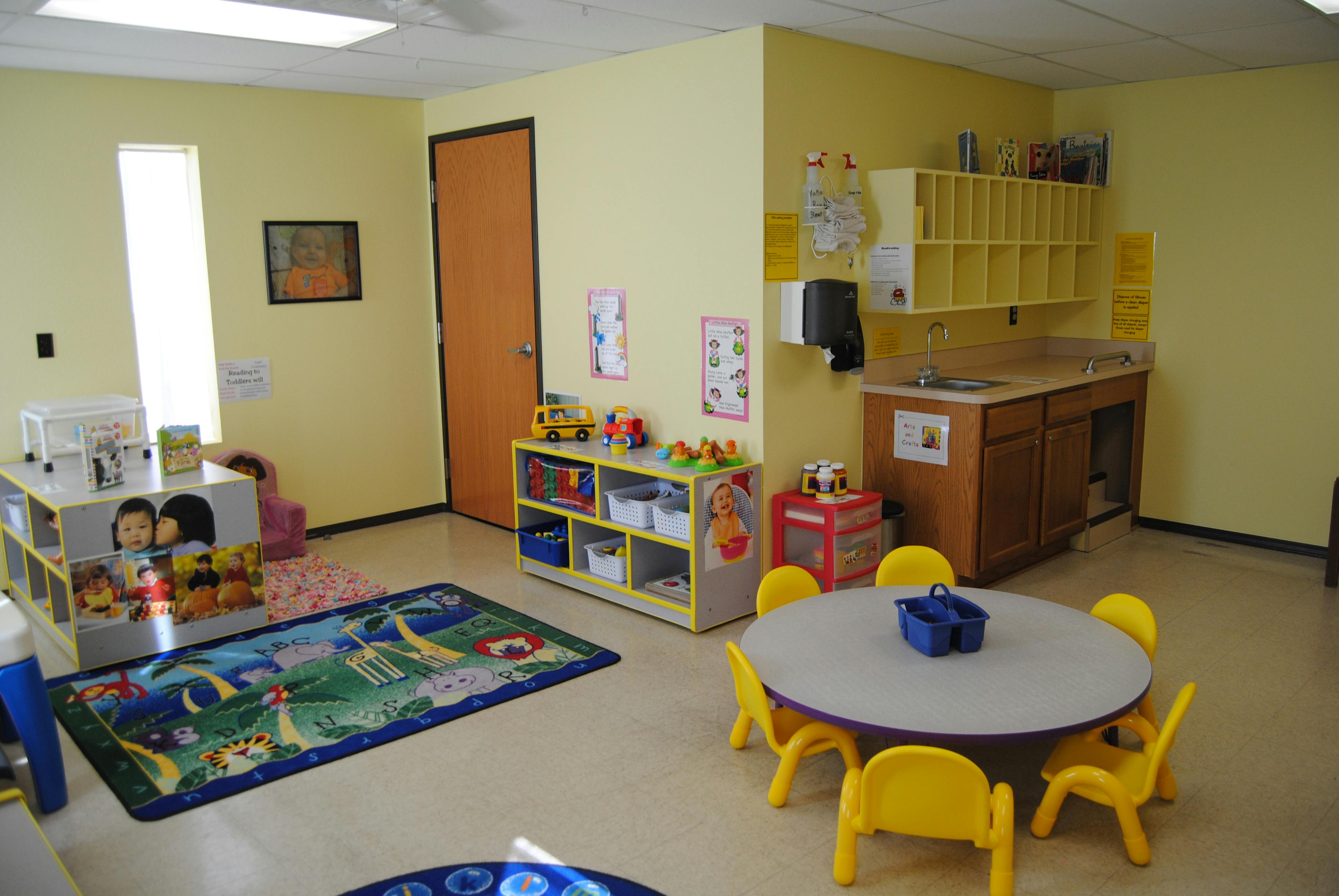 Classroom with small tables and chairs, toys, and a rug