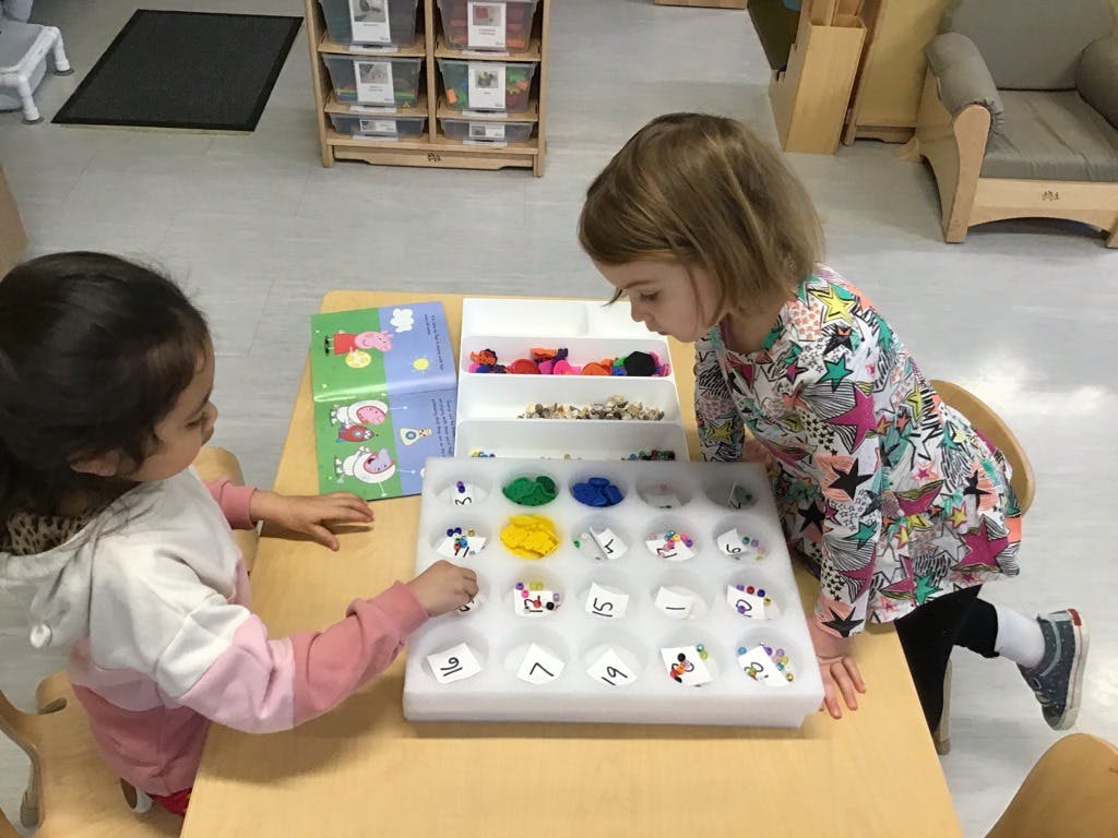 Two children playing with a sorting tray and small objects at a table