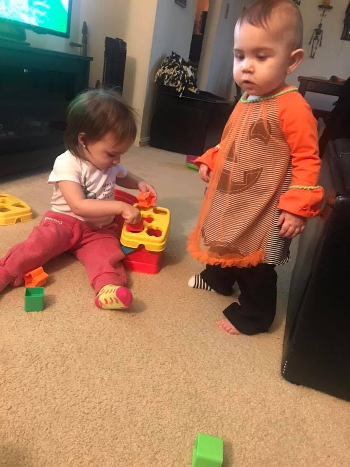 Child playing with a toy while another child stands nearby