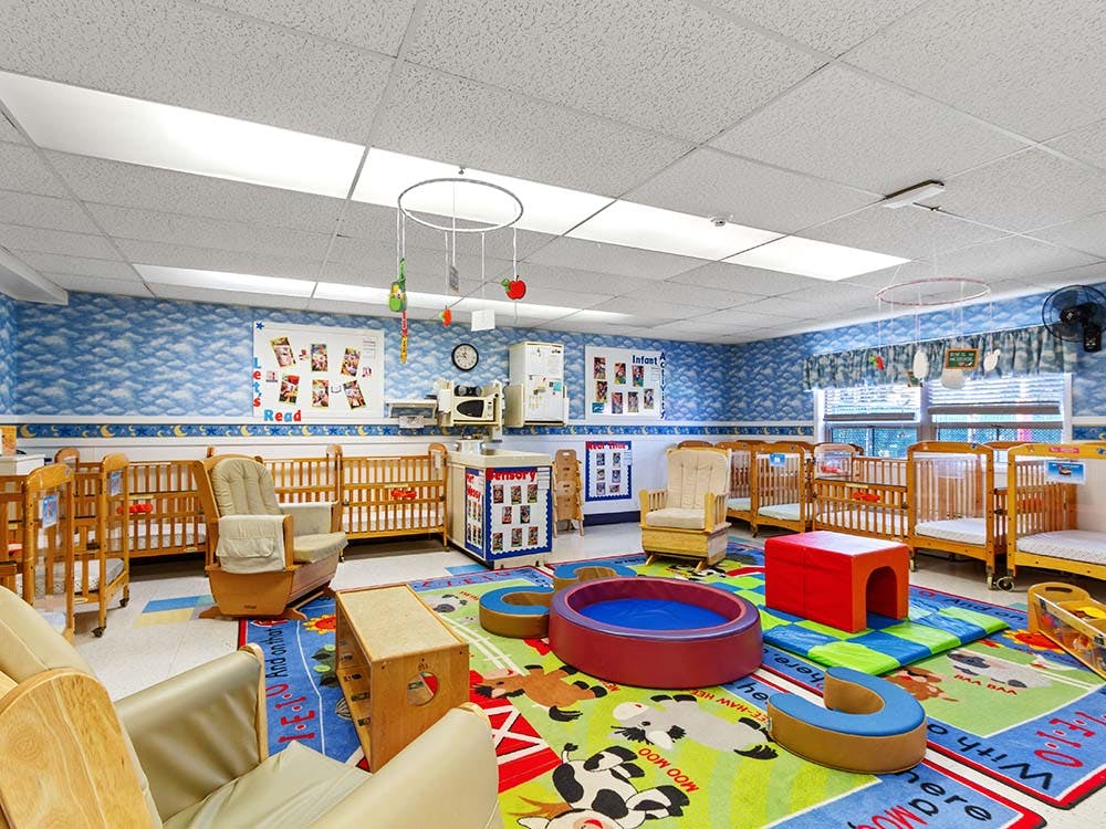 Infant nursery room with multiple cribs, a play mat, and rocking chairs