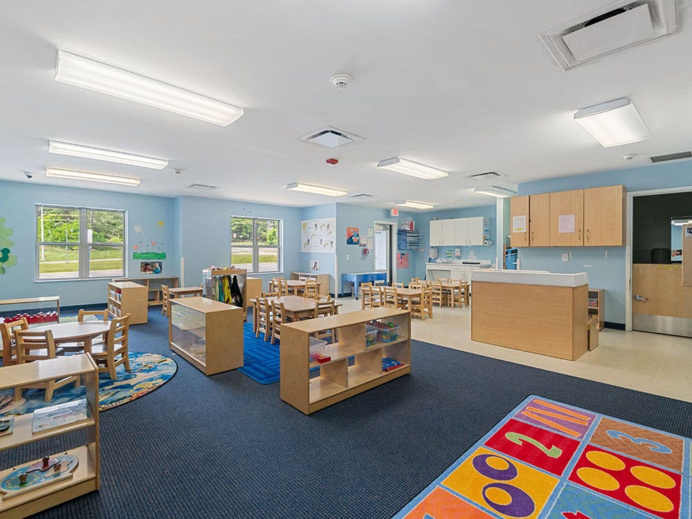 Empty preschool classroom with small tables, chairs, and learning stations