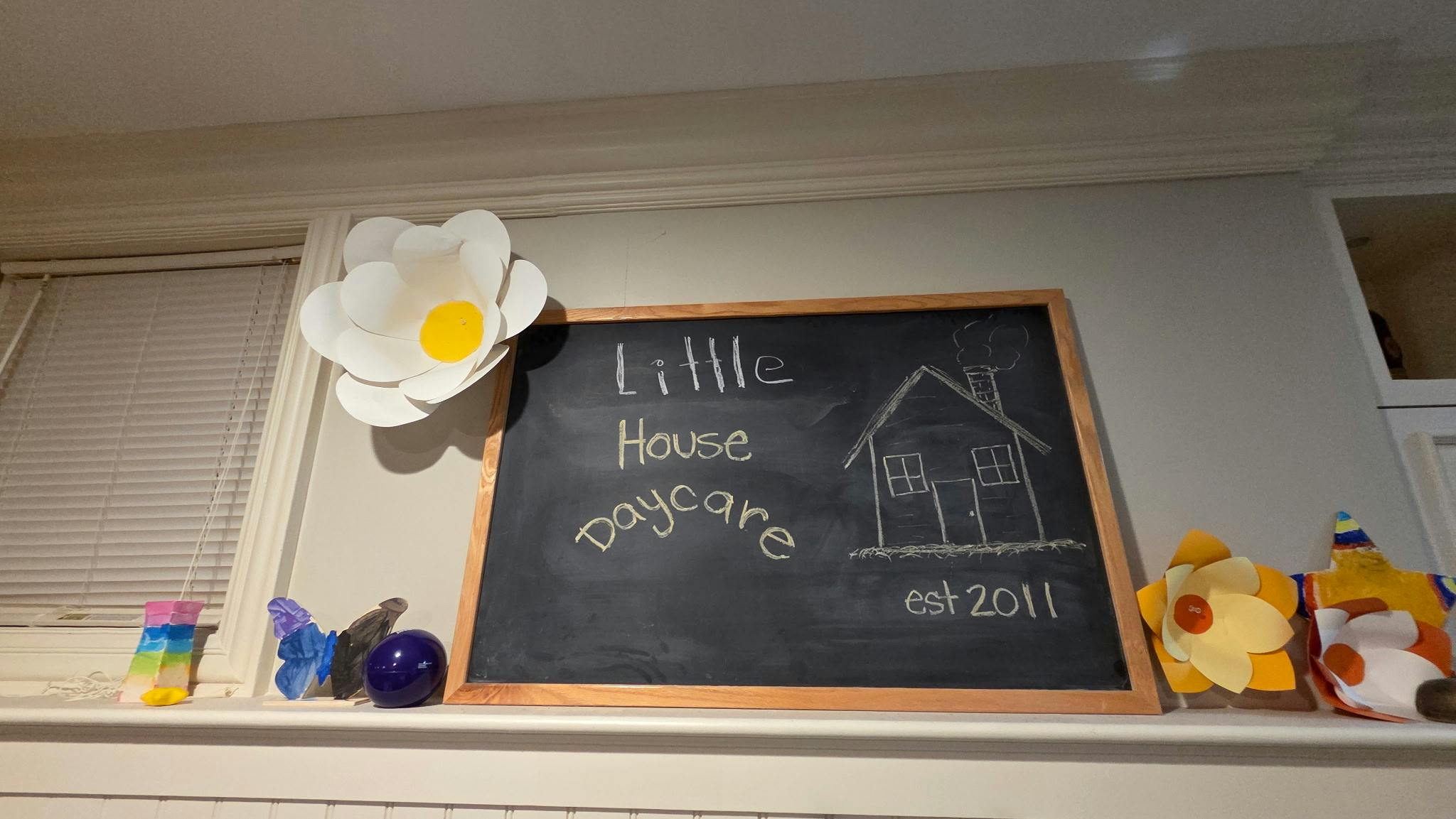 Chalkboard sign for Little House Daycare with a drawing of a house