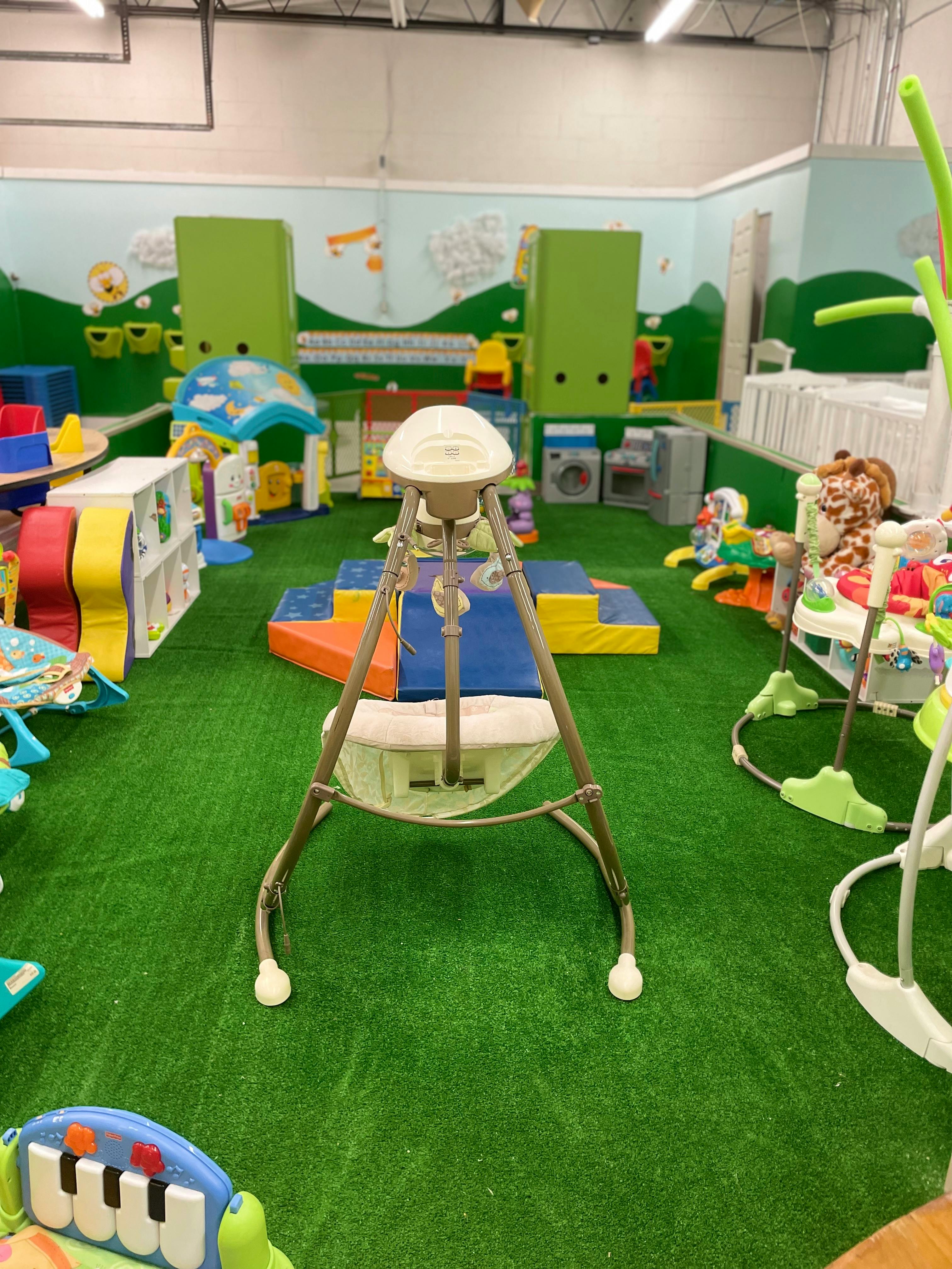 Indoor play area with various baby swings and play structures on green turf
