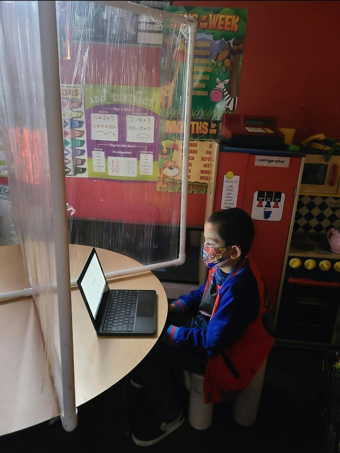 Child in a face mask sitting at a table with a laptop in a classroom