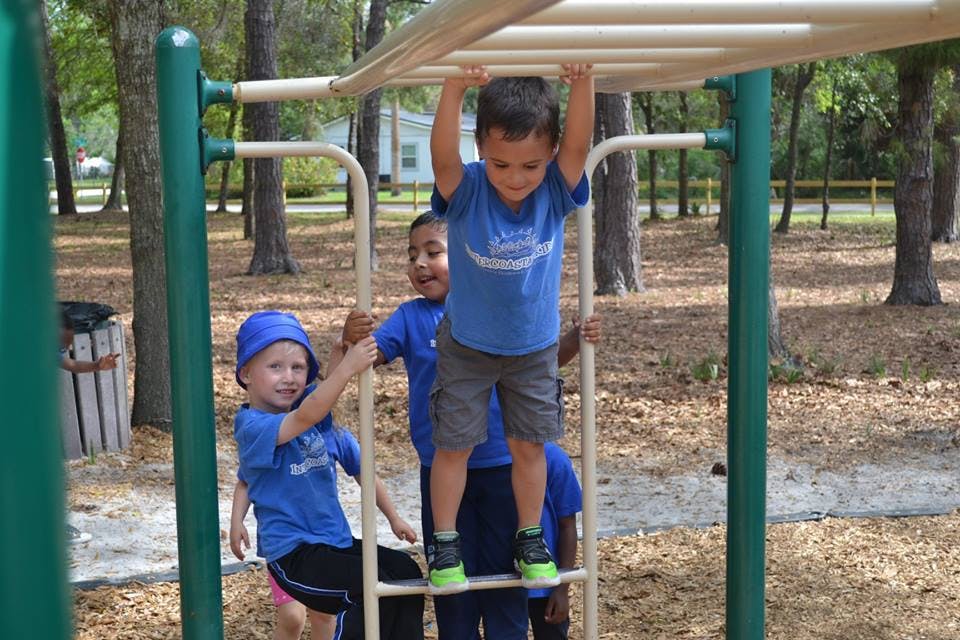 Child hanging from monkey bars with other children on playground equipment