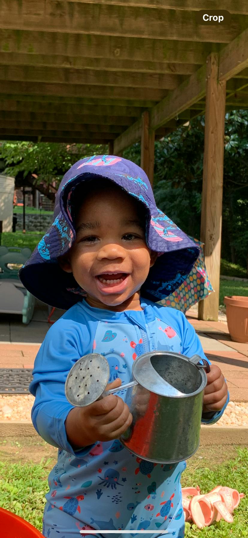 Child wearing a sun hat holding a small metal watering can