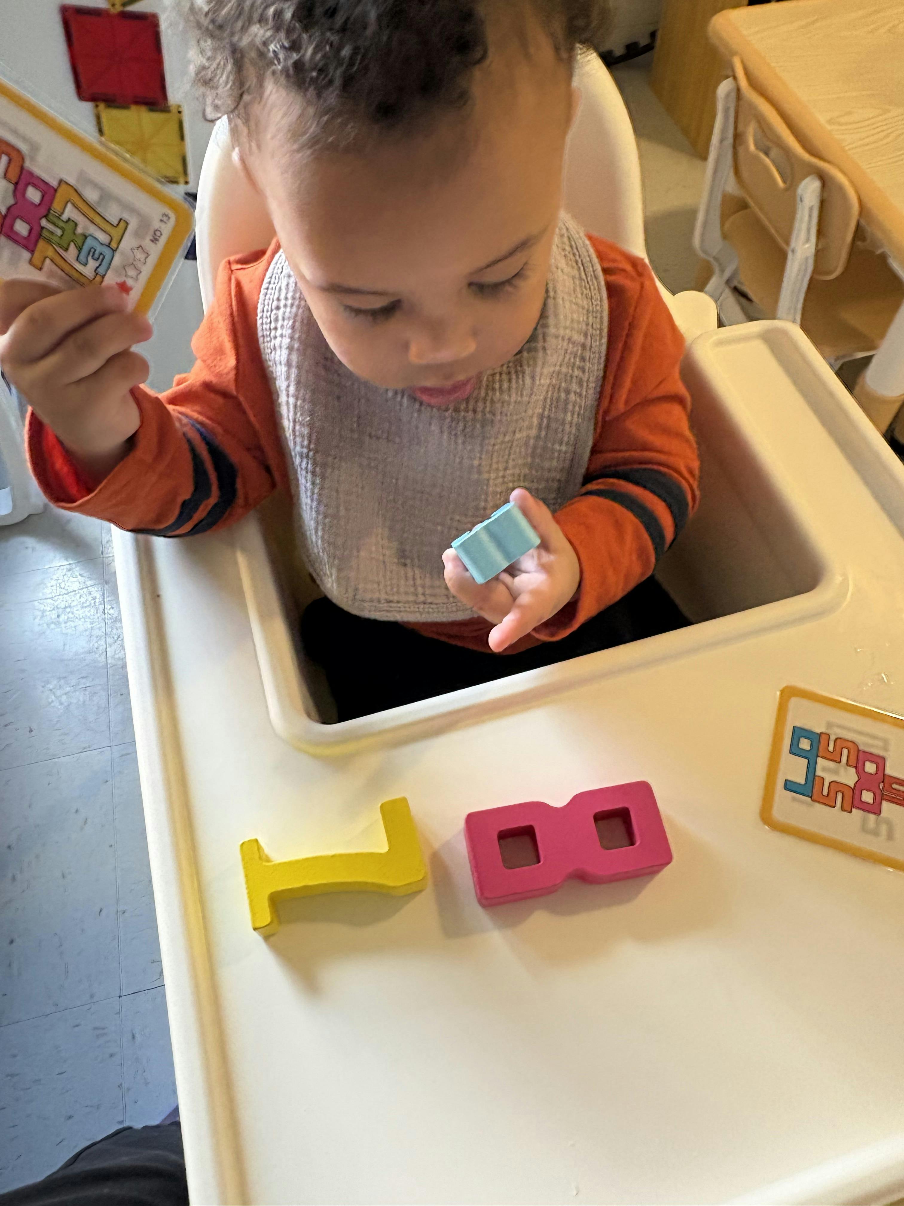 Child sitting in a high chair playing with colorful letter blocks
