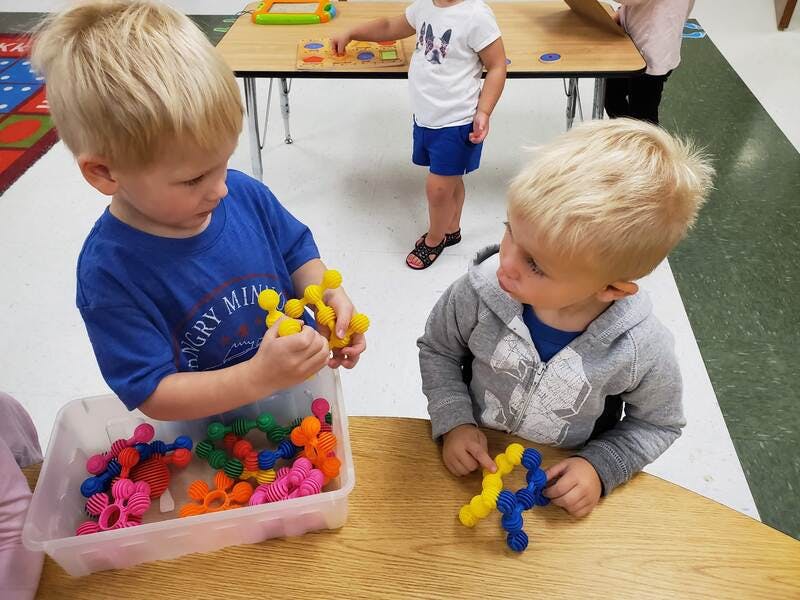 Two children playing with colorful interlocking toys at a table