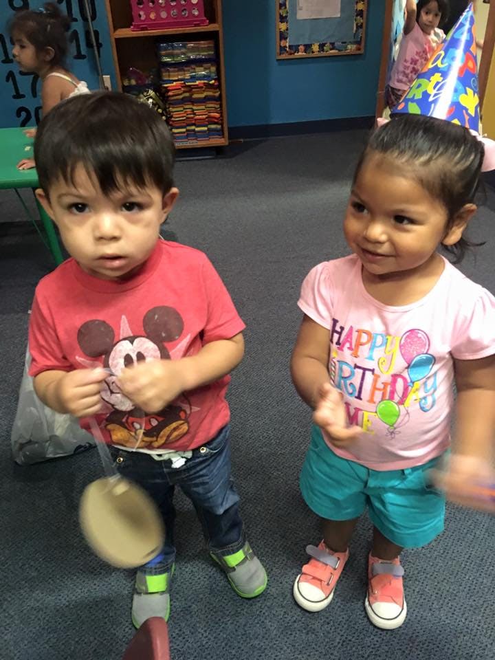 Two children standing, one wearing a party hat