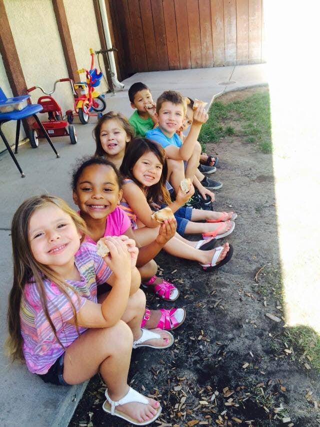 Group of children sitting in a row, some holding food