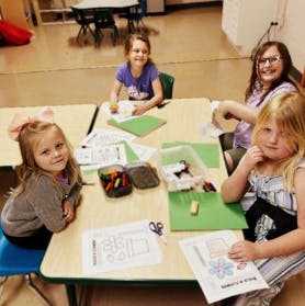 Four people at a table with craft supplies