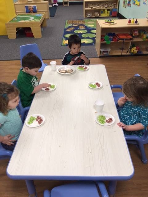 Three children eating snacks at a table in a classroom
