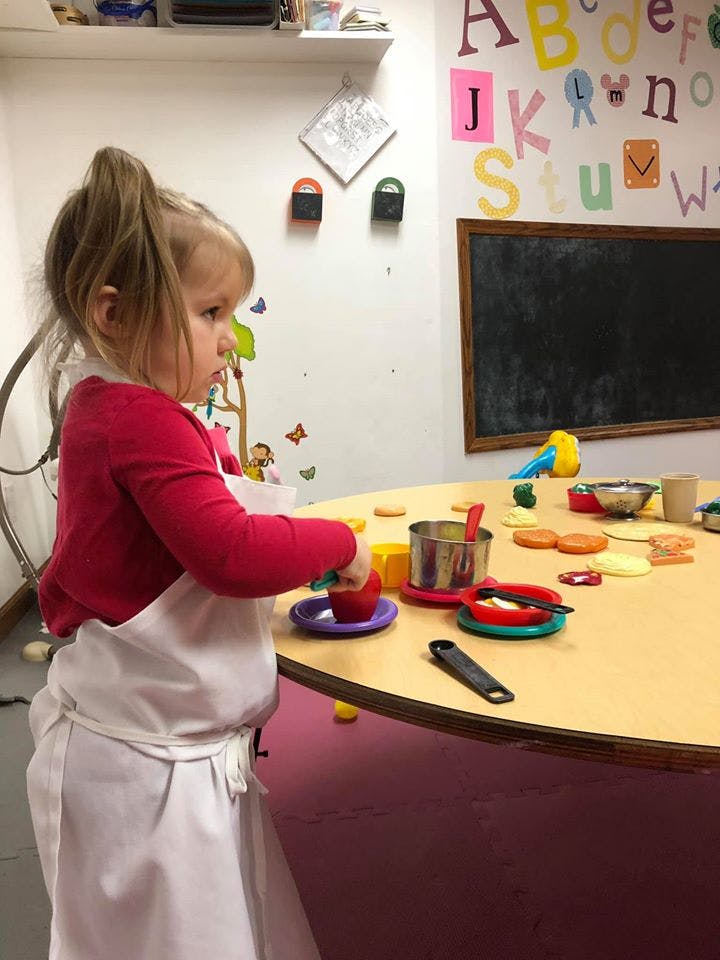 Child in an apron playing with toy kitchenware at a table