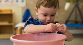 Child washing hands in a pink basin