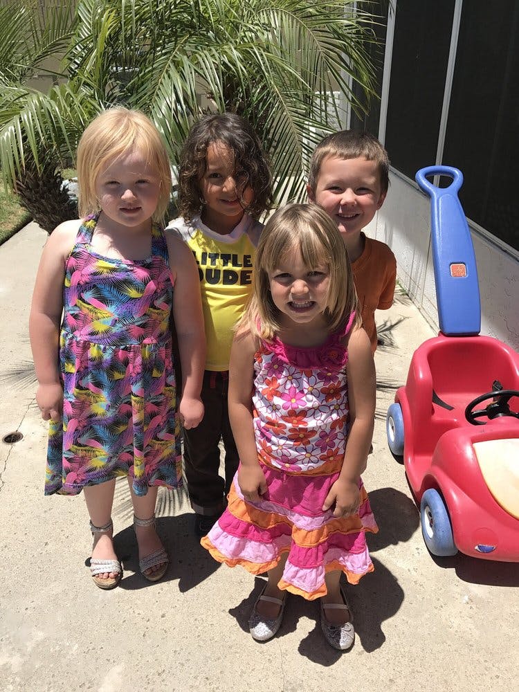 Four children standing outdoors near a red toy car