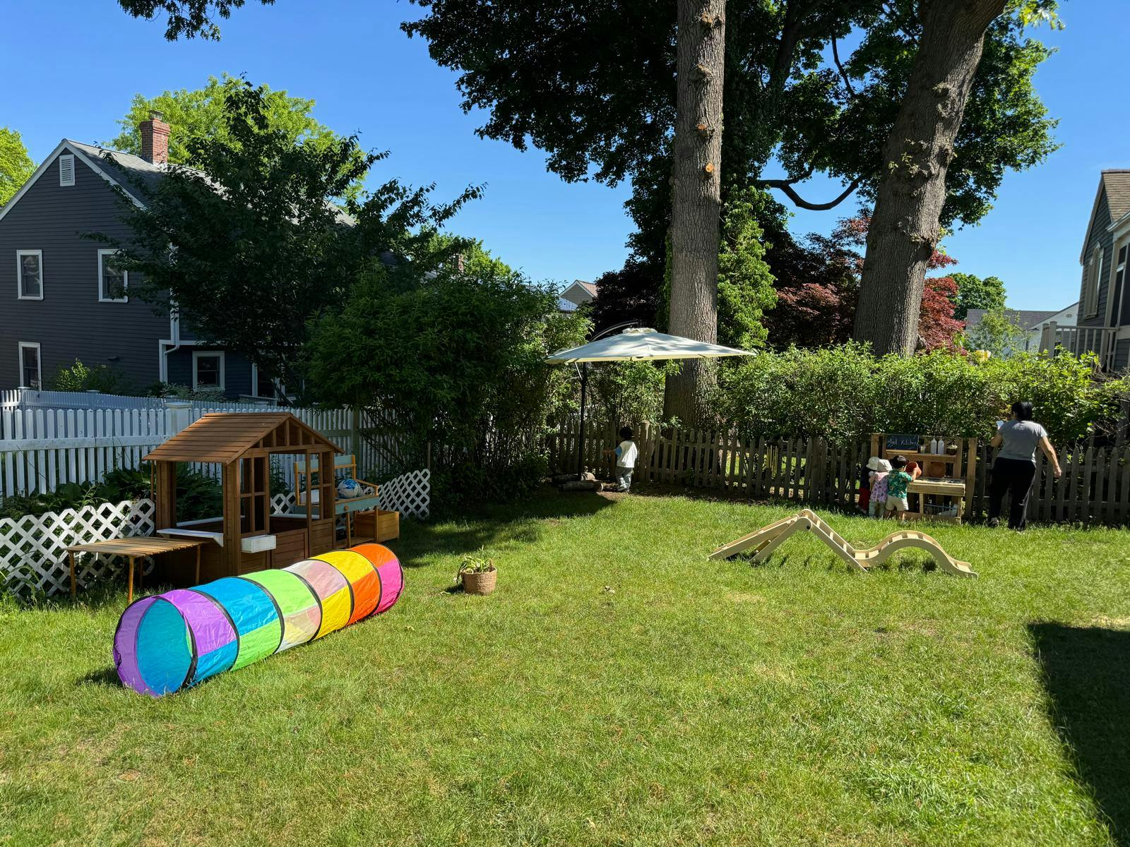 People and children playing in a sunny backyard with play structures
