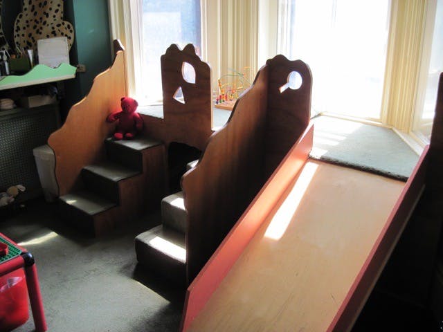 Indoor wooden playground with stairs, a red teddy bear, and a slide