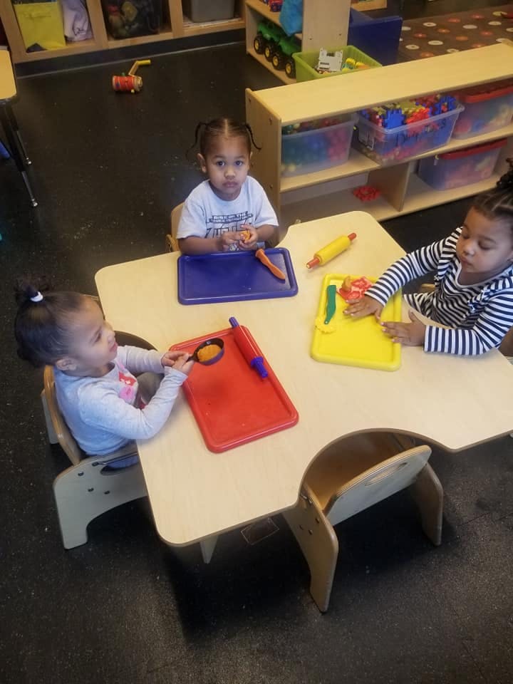 Three children at a table with play food and craft items