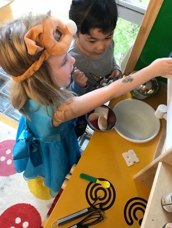 Child in a lion mask playing with a toy kitchen