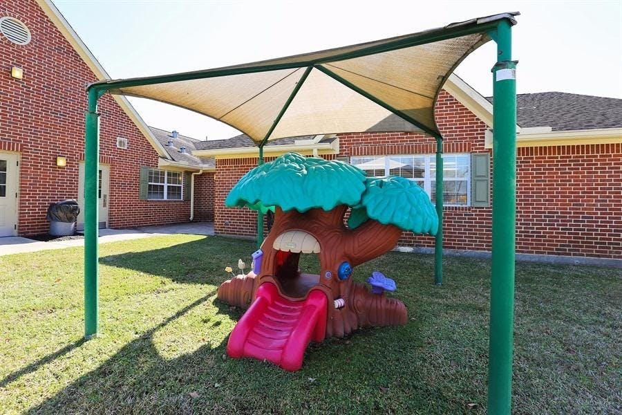 Playground with a tree-shaped play structure and red slide under a shade canopy