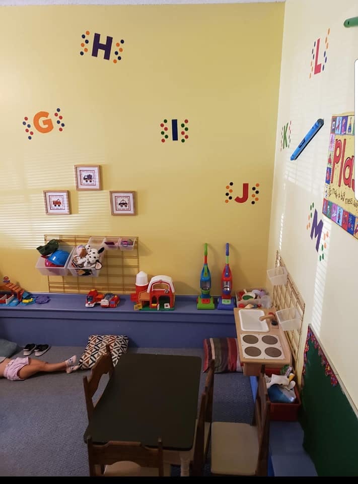 Child lying on the floor in a playroom with toys and alphabet letters on the wall