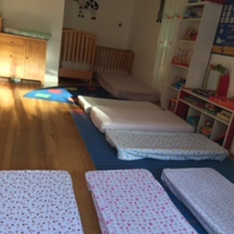 Mattresses on the floor in a room with cribs and shelves