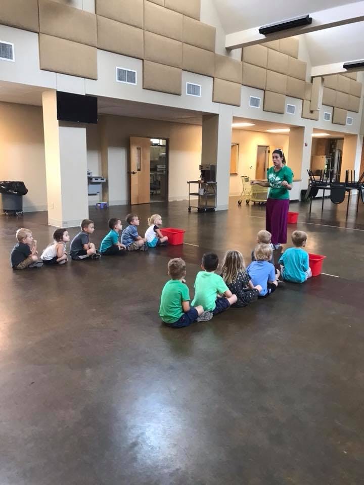 Adult person speaking to a group of children sitting on the floor